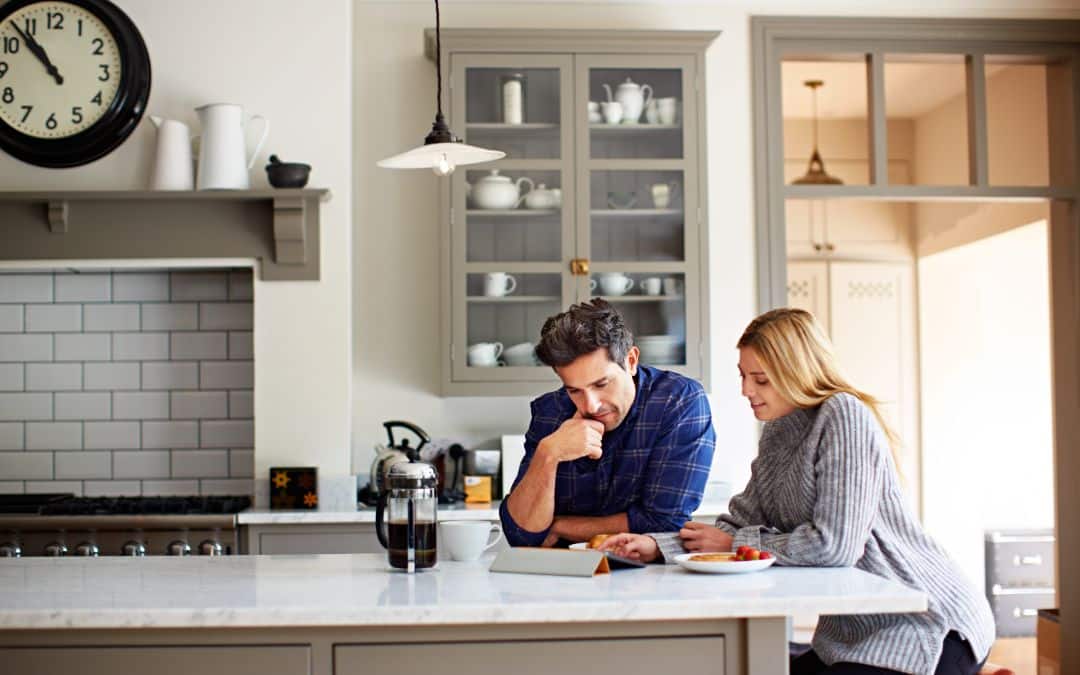 Man and women in bright, modern kitchen looking at houses on laptop. Property searches spike in January with more buyers looking to purchase a home in Four Oaks, Sutton Coldfield, UK.